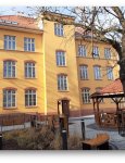 Budynek dziennego domu. Widok z dziedzińca. Żółta fasada budynku z trzema rzędami okien ze szprosami. Przed budynkiem ścieżki z kostki brukowej, duża sześciokątna altana i rabaty z krzewami